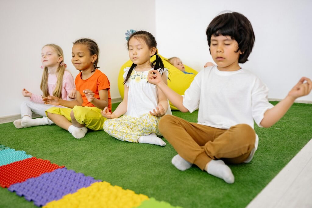 pexels-photo-8613320-8613320 Group of diverse young children meditating in yoga poses on a green mat indoors.