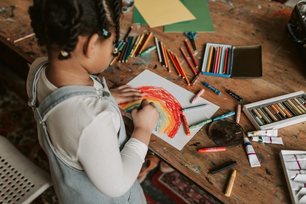 Art Therapy Young child creating a vibrant rainbow drawing at a wooden table with various art supplies in Art Therapy.